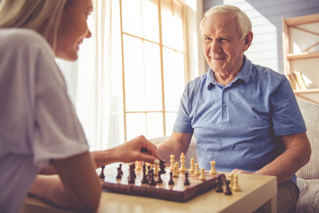 Senior Man Plays Chess with Caregiver - Open Arms Solutions