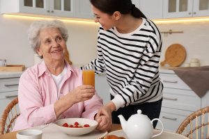 Young female caregiver serves senior woman breakfast in the kitchen