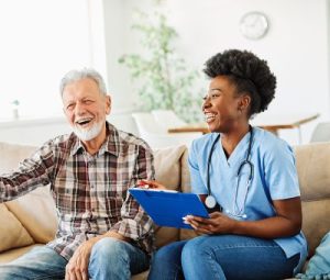 Female caregiver laughs with male senior patient on the couch