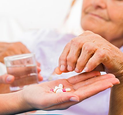 elderly patient taking medication from nurse caregiver